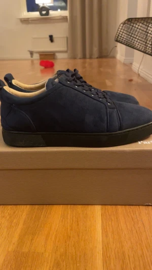 Mörkblå sneakers från Christian Louboutin - Snygga mörkblå sneakers från Christian Louboutin i mjuk mocka med svart platt sula. Skorna har rund tå och klassisk snörning, samt en stilren och minimalistisk design som passar till jeans eller chinos. Insidan är ljusbeige och ger en lyxig känsla.