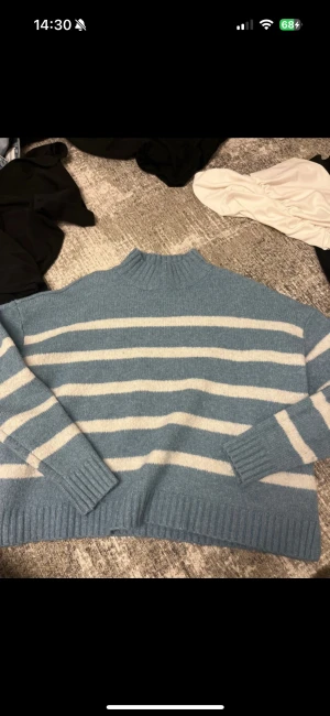 Blåvit randig stickad tröja - Mysig stickad tröja i ljusblått och vitt med breda ränder. Tröjan har ribbad polokrage, muddar och nederkant, samt långärmad passform. Perfekt för kyliga dagar och har en loose fit som ger en avslappnad vibe. Köpt i USA. Felfri