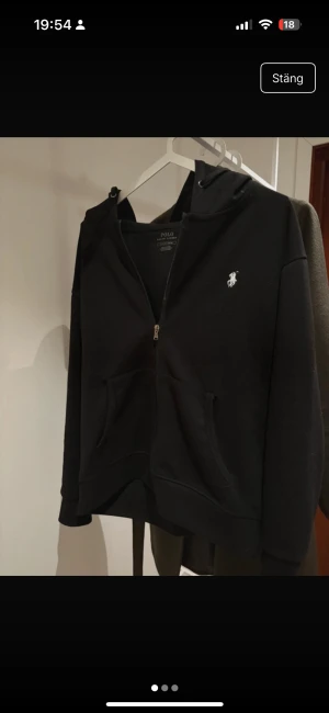 Polo Ralph Lauren - Polo Ralph Lauren – Svart Zip Hoodie (Herr/Unisex) Snygg och stilren hoodie från Polo Ralph Lauren i klassisk svart färg med det ikoniska broderade logot. Modellen har dragkedja, huva och två framfickor – perfekt till vardag, skola eller chill.