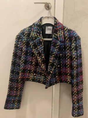 Croppad rutig kavaj från Zara - Säljer en kroppad kavaj från Zara i storlek XS. Jackan har ett färgstarkt rutigt mönster med inslag av svart, blått, rött, gult och lila, grön. Den är tillverkad i ett grovt, stickat material och har guldiga knappar framtill. Har aldrig använt. Cool kavaj, perfekt för dig som vill sticka ut!💜