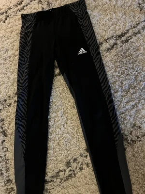 Adidas träningstights zebra 9-10 år - Jätte snygga svarta Adidas träningsbyxor med gråa delar och zebramönstrade detaljer längs sidorna. Perfekt för att sporta i. Sälja då dem tyvärr har blivit försmå💋