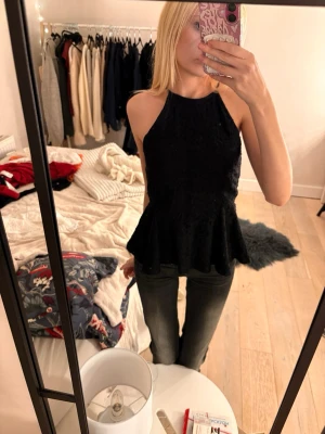 Svart spetsig blus med volang - Supersnygg svart blus från Gina tricot med spets och volang nertill. Modellen är ärmlös med hög hals och har en feminin, peplum-liknande siluett. Perfekt för dig som gillar detaljer och vill ha en chic look. Spetsen ger en extra touch och blusen är lätt att matcha.