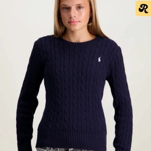 Marinblå kabelstickad tröja Polo Ralph Lauren - Snygg marinblå kabelstickad tröja från Polo Ralph Lauren med klassisk rund hals och vit broderad logga på bröstet. Tröjan har långärmad passform och ribbade muddar vid ärmslut och nederkant. Köpt för 1695kr andvönd ca 3 gånger 