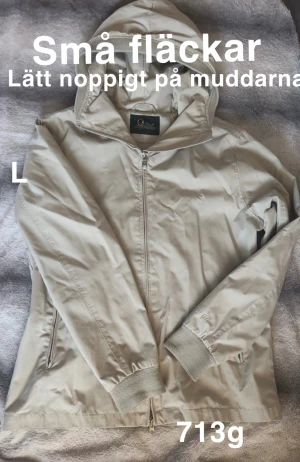 Beige vindjacka Peak Performance L - Beige vindjacka från Peak Performance med huva och dragkedja framtill. Jackan har ribbade muddar vid ärmslut och två fickor med dragkedja. Perfekt för blåsiga dagar och enkel att matcha med det mesta.🌸 Små fläckar. Lätt noppig på muddar och kragen. Storlek L