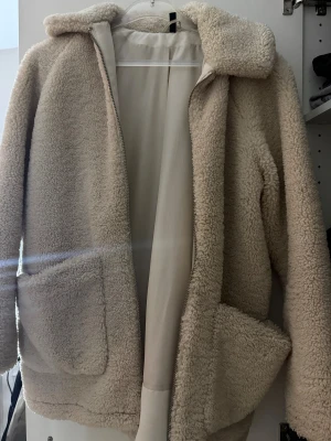 Beige teddyjacka från H&M Divided S - Mysig beige teddyjacka från H&M Divided i storlek S. Jackan har dragkedja framtill, två stora fickor och en mjuk, fluffig känsla. Perfekt för kyliga dagar och ger en chill vibe till din outfit. Finns en liten fläck men går bort i tvätten.
