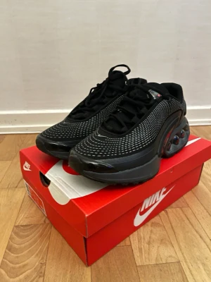 Nike Air Max DN svarta sneakers - Nike Air Max DN sneakers i svart med vita prickdetaljer och futuristisk design. Skorna har en chunky platt sula med synliga Air Max-bubblor, snörning och rund tå. Ovandelen är i syntet och mesh för bra ventilation. Perfekt för dig som gillar streetwear och sportig stil. Passar 41-42