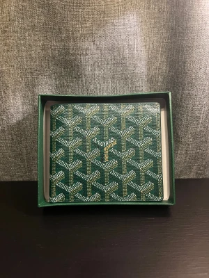 Grön plånbok med mönster - Säljer en grön plånbok med det klassiska grafiska mönstret i vitt och gult. Plånboken är tillverkad i skinn och har flera fack för kort. Märket och 'Made in France' är präglat på insidan. Kommer i original ask med logga.