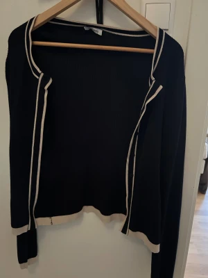 Marinblå  ribbad kofta med vit kant - Marinblå  ribbad kofta från Happy Holly med vit kant längs halsringning, knappslå och nederkant. Långärmad modell med smala svarta knappar framtill. Snygg och stilren, perfekt för lager-på-lager. 