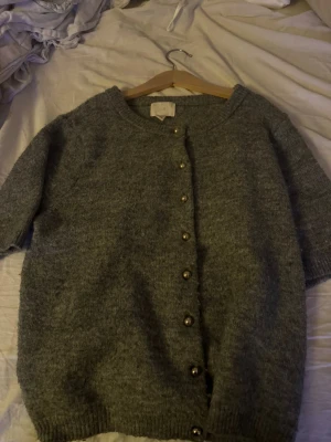 Grå stickad kofta från H&M - Mysig grå stickad kofta från H&M med korta ärmar och rund hals. Den här guldiga knappar💗