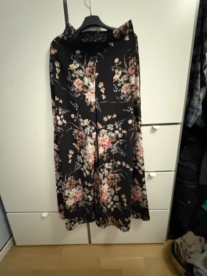 Blommiga wide byxor från SHEIN - Svarta byxor med blommigt mönster i rosa, beige och vitt från SHEIN. Modellen är wide med hög midja och har ett flowigt, luftigt tyg som ger en snygg siluett. Perfekta för dig som gillar statement-plagg och vill sticka ut med en cool look.