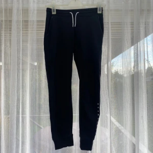 Svarta mjukisbyxor med snörning - Svarta mjukisbyxor med vit snörning i midjan och diskret tryck längs ena benet. Byxorna har muddar vid bensluten och sidofickor, perfekta för en chill och avslappnad stil.