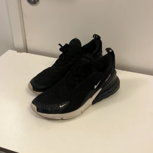 Nike Air Max 270 svarta sneakers - Svarta Nike Air Max 270 sneakers med vit sula och röda detaljer undertill. Skorna har en luftig mesh-överdel, tydlig Air Max-dämpning i hälen och klassisk Nike-logga på sidan. Perfekta för dig som gillar sportig stil och vill ha bekväma skor med snygg design.