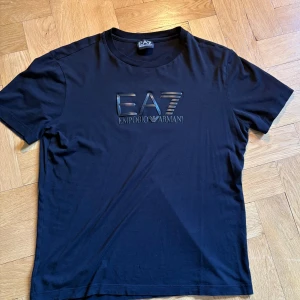 Svart EA7 Emporio Armani t-shirt - Säljer en riktigt skön ea7 T-Shirt. Skicket är 8/10 därför jag säljer den rätt billigt, inga defekter. Tveka inte att skriva ifall du har några frågor eller funderingar 