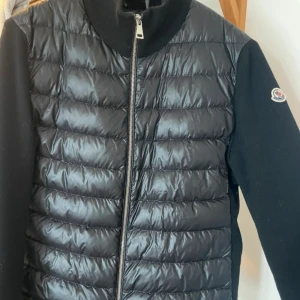 Svart Moncler Cardigan - Säljer min svarta Moncler cardigan då den tyvärr inte kommer till användning. I storlek M men passar även S. Inga defekter och ser helt som ny ut. Kan även mötas upp
