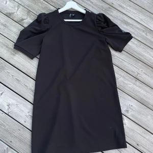 Svart kort puffärmad klänning Vero Moda - Svart kortklänning från Vero Moda med puffiga korta ärmar och rund halsringning. Enkel och stilren design i ett mjukt, slätt material som känns bekvämt. Perfekt för dig som gillar minimalistisk stil med en twist.