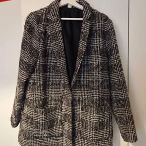 Rutig kappa i svart och vitt - Säljer en snygg rutig kappa i svart och vitt med klassisk krage och två stora fickor framtill. Jackan har använts men har int3 defekter 