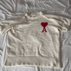 Vit stickad tröja från Ami Paris - Vit stickad tröja från Ami Paris med röd hjärtlogga och bokstaven A på bröstet. Tröjan har ribbade muddar vid hals, ärmslut och nederkant. Klassisk passform och rund halsringning, perfekt för lager-på-lager. Riktigt fet till vintern och passar till allt! Tags följer med! Pris kan ändras på snabb affär! Tröjan kan förstoras och förminskas vilket gör att den passar S och M