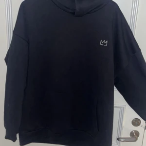 Svart Hov1 hoodie XL med krona - Säljer en svart hoodie från Hov1 i storlek XL. Framtill finns en liten broderad krona och på ryggen står det 'Vi Dansar Vidare I Livet' med turnédatum. Hoodien har huva och magficka,  säljer då den inte kommer till användning, använd några få gånger, priset går att diskutera 💕💕(den sitter helt okej på mig som vanligt vis har S)