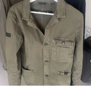 Olivgrön overshirt  - Olivgrön overshirt från Superdry med klassisk krage, tre fickor framtill och knäppning med knappar. 