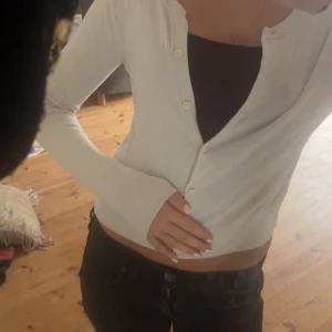 Vit kofta från H&M i XS - Snygg vit kofta från H&M i storlek XS. Modellen är croppad med långa ärmar och knappar framtill. Perfekt att slänga över ett linne eller topp. Enkel och stilren design som passar till det mesta.