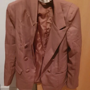 Kavaj - Dubbelknäppt brun kavaj i storlek M. Klassisk modell med breda slag, två fickor med lock och knappar framtill. Perfekt för dig som vill ha en stilren och trendig look. Materialet känns mjukt och har en snygg finish.