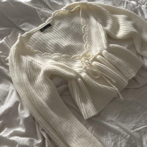 Vit stickad kofta med snörning från SHEIN - Supersöt vit stickad kofta från SHEIN med långa ärmar, volangkant vid halsringningen och snörning framtill. Koftan är croppad och har en mysig, ribbad struktur som ger en trendig vibe. Perfekt att slänga över en topp för en chill look.