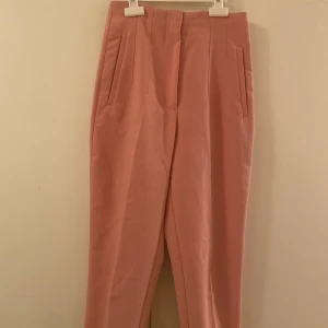 Rosa kostymbyxor med raka ben - Snygga ljusrosa kostymbyxor med hög midja och raka ben. Byxorna har diskreta fickor i sidorna och stängs framtill. Perfekta för en clean och stilren look, passar till både sneakers och klackar. Materialet känns mjukt och har en lätt stretch. Den är i storlek XS, hör av er ifall ni har några frågor🩷🩷