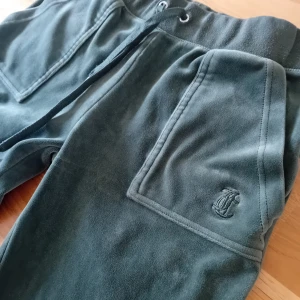 Juicy couture velourbyxor XS mörkgröna - Mörkgröna mjukisbyxor i mjuk velour med bred resår i midjan och snörning. Stora framfickor och bakfickor med lock och knappar. Fint begagnat skick!