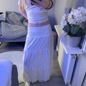 Vit långkjol med volanger - Säljer en vit långkjol med bred smock i midjan och flera volanglager. 