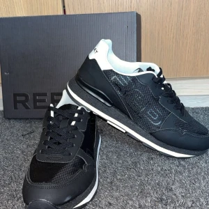 Svarta sneakers från Replay - Snygga svarta sneakers från Replay med vita detaljer och logga på hälen och sulan. Ovandelen har meshpaneler och syntetmaterial, samt snörning framtill. Sulan är svart med vita inslag och har en sportig look. Perfekta för en trendig streetstyle. Jag köpte de på 1000. Säljer de för 800 då de inte passar mig det är storlek 42 aldrig använt 