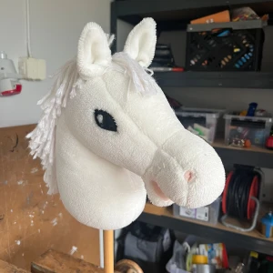 Käpphäst - Bilderna visar en vit käpphäst med mjuk plysch och garnman, perfekt för lek och hobby. Den har broderade svarta ögon och detaljerad nos. Passar dig som gillar hästar och vill ha kul med vänner eller träna trick. Snygg och stilren design som gör den till ett roligt inslag i vardagen. Fleece skulle jag tro att materialet är. Jag har köpt käpphästen på Panduro och gjort man och ögon och sytråd själv.