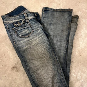 Lågmidjade blå jeans  - Säljer ett par snygga lågmidjade jeans i ljusblå tvätt med slitna detaljer och coola fickor fram. Jeansen har klassisk femficksdesign och sitter tight över höfterna. Perfekta för dig som gillar en avslappnad men trendig look.