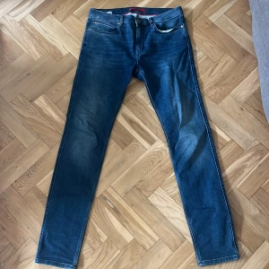 Hugo Boss jeans - Snygga blå jeans från Hugo Boss med klassisk femficksdesign och diskret logga på bakfickan. Jeansen har en slim passform och är tillverkade i stretchigt denim för extra komfort.