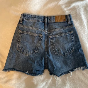 Blå jeansshorts  - Snygga blå jeansshorts från 157 med hög midja och fransiga kanter. Klassisk femficksmodell med bälteshällor och knappstängning. Perfekta för sommardagar 