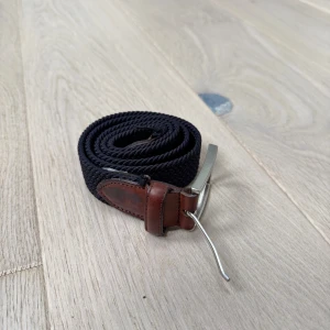 Flätat Bomullsbälte - 90 cm - Säljer ett mörkblått flätat bomullsbälte från Saddler (90 cm). Köpt på Volt för ett år sedan, nypris ca 600 kr.