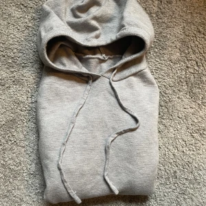 Grå Merinoull hoodie - Säljer en stilren grå hoodie med huva och snörning. Perfekt för chill dagar eller när du vill ha något bekvämt och enkelt. Mjuk och skön känsla, passar till det mesta. Snygg basic som alltid funkar.