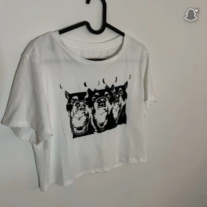 Vit t-shirt med svart tryck - Vit t-shirt med coolt svart tryck av tre hundar på bröstet. Modellen är croppad med rund hals och korta ärmar, perfekt för dig som gillar streetstyle och grafiska motiv. Materialet känns mjukt och lätt, troligen bomull. Storlek XL men liten i storleken. 