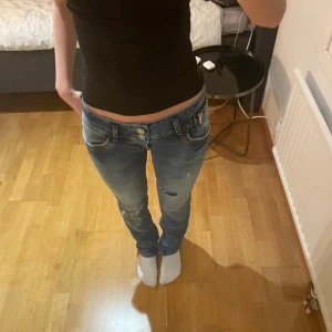 Blå skinny jeans med slitningar - Säljer ett par blå skinny jeans från LTB med låg midja och slitna detaljer på benen. Jeansen har dubbla knappar i midjan, dragkedja vid fickan och snygga bakfickor med gul söm. Perfekta för dig som gillar en avslappnad och trendig look.