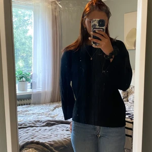 Svart stickad långärmad tröja - En svart stickad tröja med lång ärm och enkel design. Tröjan har en normal passform och är perfekt att bära till jeans eller andra favoritplagg. Mjuk och skön känsla, passar dig som gillar stilrena och klassiska plagg.