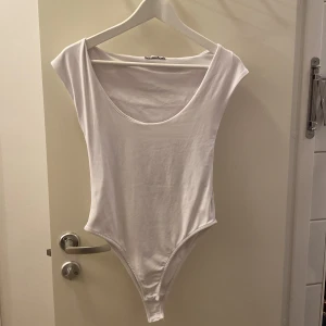 Vit bodysuit från Zara - Säljer en vit bodysuit från Zara,Modellen har djup rundad urringning fram, ärmlös design och smal passform som sitter snyggt mot kroppen. Perfekt att styla med jeans eller kjol för en clean look. Bodysuiten är aldrig använd