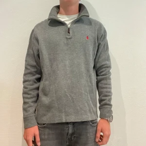 Grå half zip tröja från Polo Ralph Lauren - Grå Polo Ralph lauren tröja i storlek S. Den är i bra skick utan några defekter. Grabben på bilden är 170 cm och 60 kg. Tveka inte på att höra av dig vid minsta fråga eller fundering.