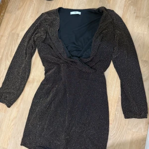 Glittrig svart kortklänning från ASOS - Den här klänningen suppersny sitter tajt i midjan och är långarmad har en öppen framsidan och finns i storlek M