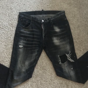 Svarta Dsquared2  jeans med slitningar - Säljer ett par svarta slim fit jeans från Dsquared2 med coola slitningar och trasiga detaljer på benen. Jeansen har en tvättad look med ljusa partier. Vid snabbaffär kan priset sänkas en bra del!