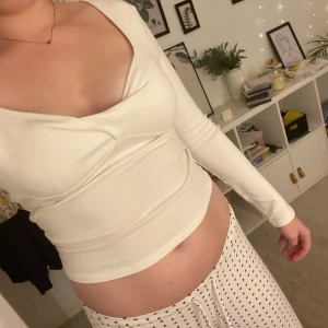 Vit långärmad topp med v-ringning - Säljer en stilren vit långärmad topp med snygg v-ringning och figurnära passform. Toppen har en lätt croppad längd och är tillverkad i mjuk bomullsmix som känns skön mot huden. 