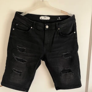 Jeansshorts FSBN - Strl M - Svarta jeansshorts från FSBN med slitna detaljer och uppvikta benslut. Shortsen är i mycket bra skick och är i klassisk femficksmodell med knapp och dragkedja framtill. 