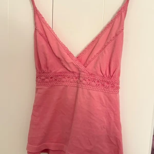 Rosa vintage topp med spets - Supersöt rosa vintage topp med omlott-skärning och smala axelband. Toppen har fina spetsdetaljer längs urringningen och midjan, samt knytband i ryggen för extra snygg passform. Står M men passar mer mot XS/S hållet skulle jag säga! 🙌🏼 Hör av er vid frågor!💞