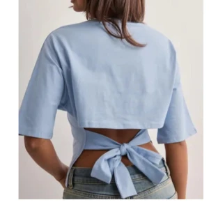 Ljusblå croppad topp med knyt - Superfin ljusblå croppad topp med öppen rygg och bred knytning i midjan. Toppen har korta ärmar och en avslappnad passform, perfekt till jeans eller kjol för en cool look.
