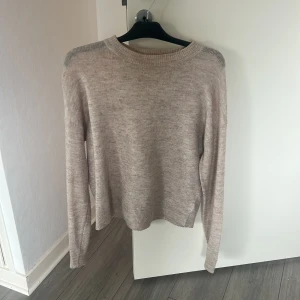 Beige stickad tröja med rund hals - En stilren beige stickad tröja med rund halsringning och långa ärmar. Tröjan har en mjuk känsla och ribbade muddar vid ärmslut och nederkant. Perfekt för lager-på-lager och enkel att matcha med jeans eller kjol.