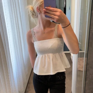 superfin topp från Gina Tricot - Supersöt vit topp från Gina Tricot i storlek XS. Toppen har smockad överdel, volang nertill och spetsiga axelband. Perfekt för varma dagar och ger en romantisk vibe till din outfit. Knappt använd. 