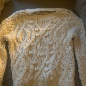 Vit stickad tröja från Bik Bok - Supermysig vit stickad tröja från Bik Bok i chunky garn med flätstickat mönster och bollar framtill. Tröjan har lång ärm och rund halsringning, perfekt för kalla dagar! St xs men passar även s